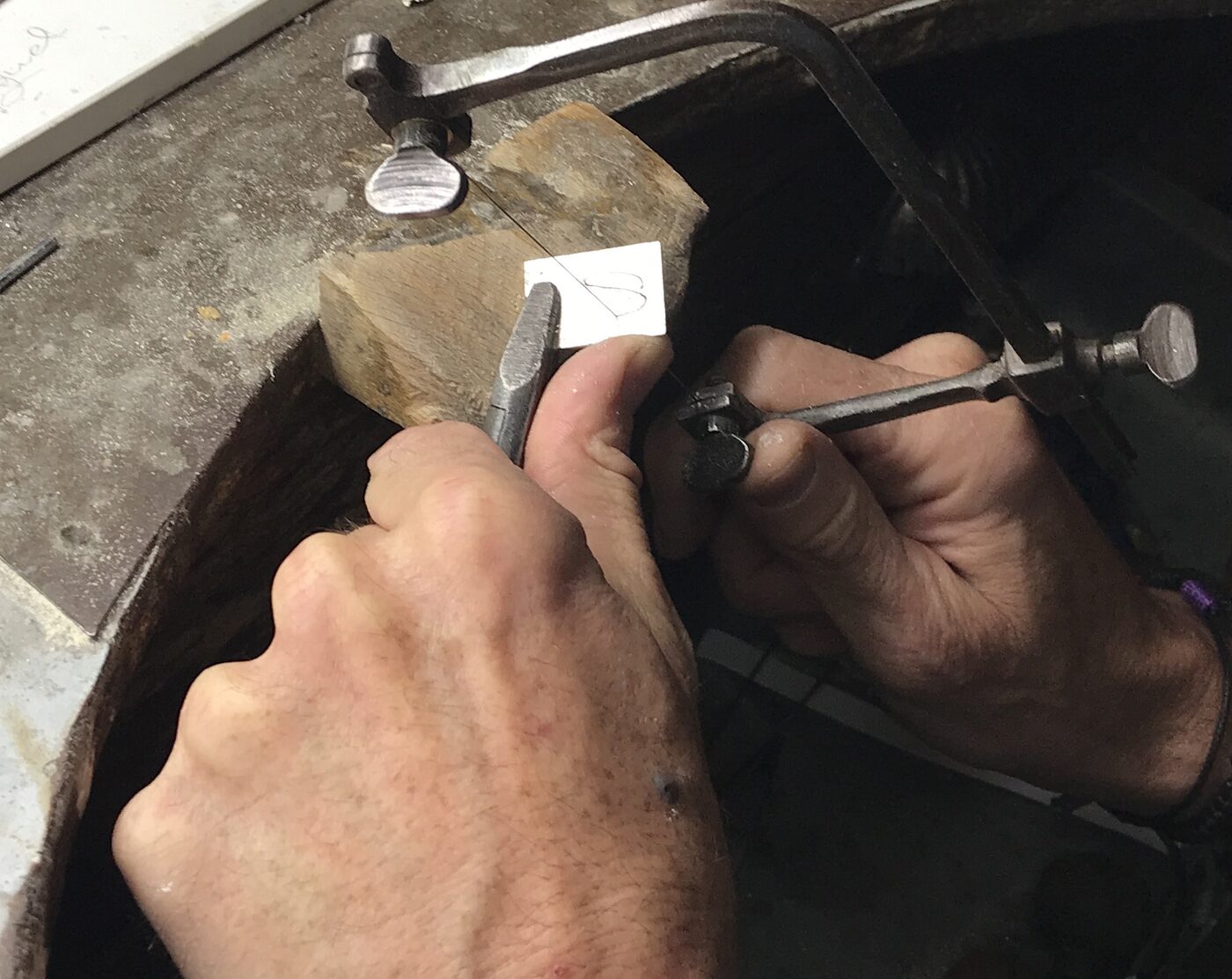 Manos del joyero cortando metal con una sierra en el banco de trabajo